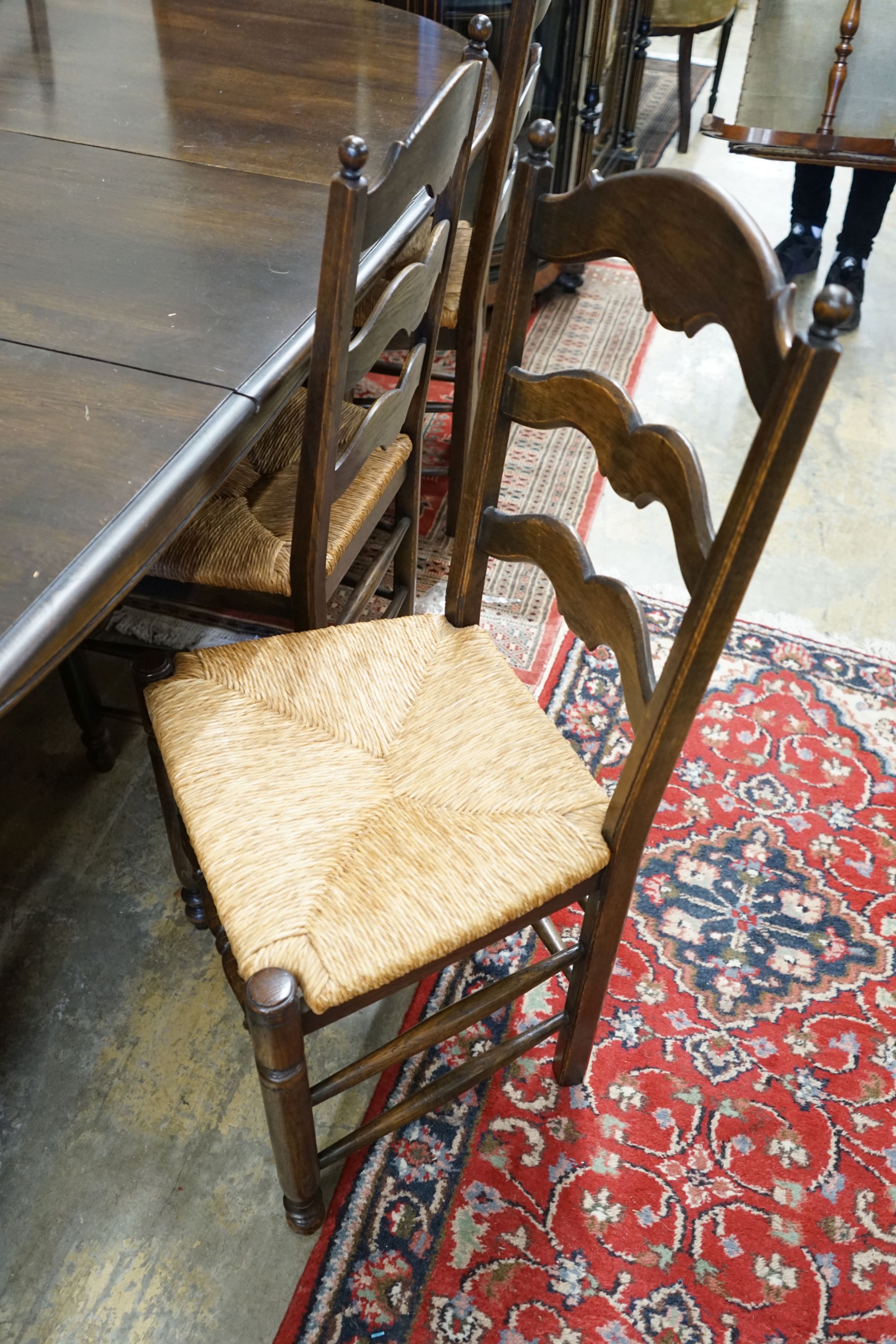 A French style oak extending dining table, with two spares leaves, 280cm extended, width 11cm, height 74cm together with a set of ten ladder backed rush seated chairs